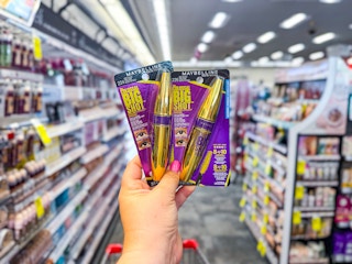 person holding 2 maybelline mascaras in an aisle