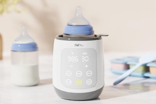 A bottle warmer sits on a counter with an extra bottle and other baby items