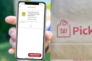 hand holding a smartphone with a walgreens cash booster coupon on it in front of a brown walgreens pickup bag