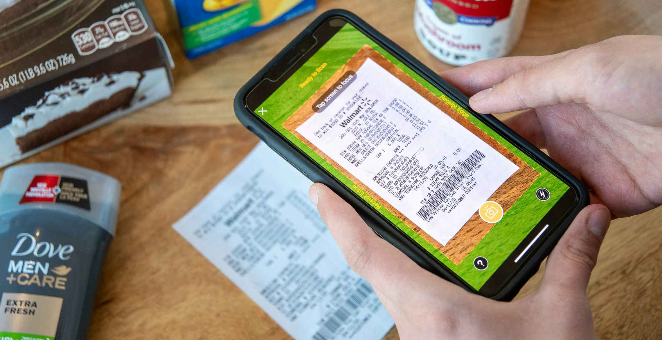A person’s hands holding an iPhone with the Fetch mobile app open to the receipt-scanning feature. The user is centering the phone’s ...