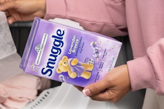 Woman throwing dryer sheet into dryer and holding box