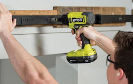 a person drilling in a nail on a piece of wood on a wall