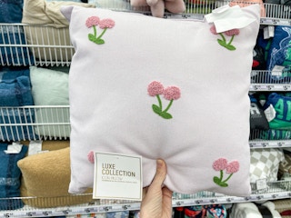 A Throw pillow held out by hand in front of a shelf full of other throw pillows