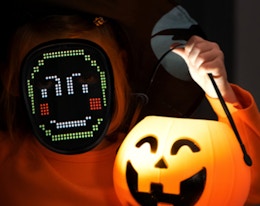 a kid with a LED mask holding a Halloween pumpkin bucket
