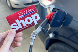 someone holding a costco shop card next to a car being filled with gas