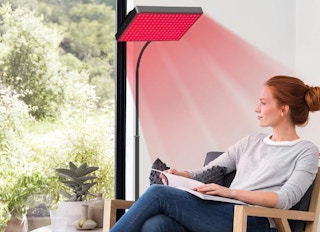 a person sitting under a red light therapy lamp