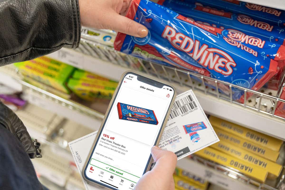 A person taking a bag of RedVines from a shelf at Target, while holding their cellphone displaying a coupon for 15% off RedVines, and a p...