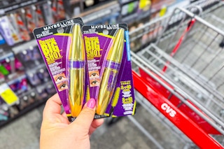 person holding 2 maybelline mascaras by a cvs cart