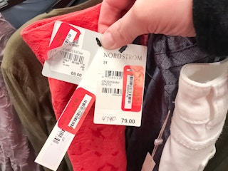 A person holding three price tags all with Nordstrom on the tag along with 3 red price tag stickers for Nordstrom Rack.
