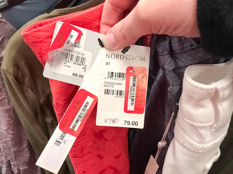 A person holding three price tags all with Nordstrom on the tag along with 3 red price tag stickers for Nordstrom Rack.