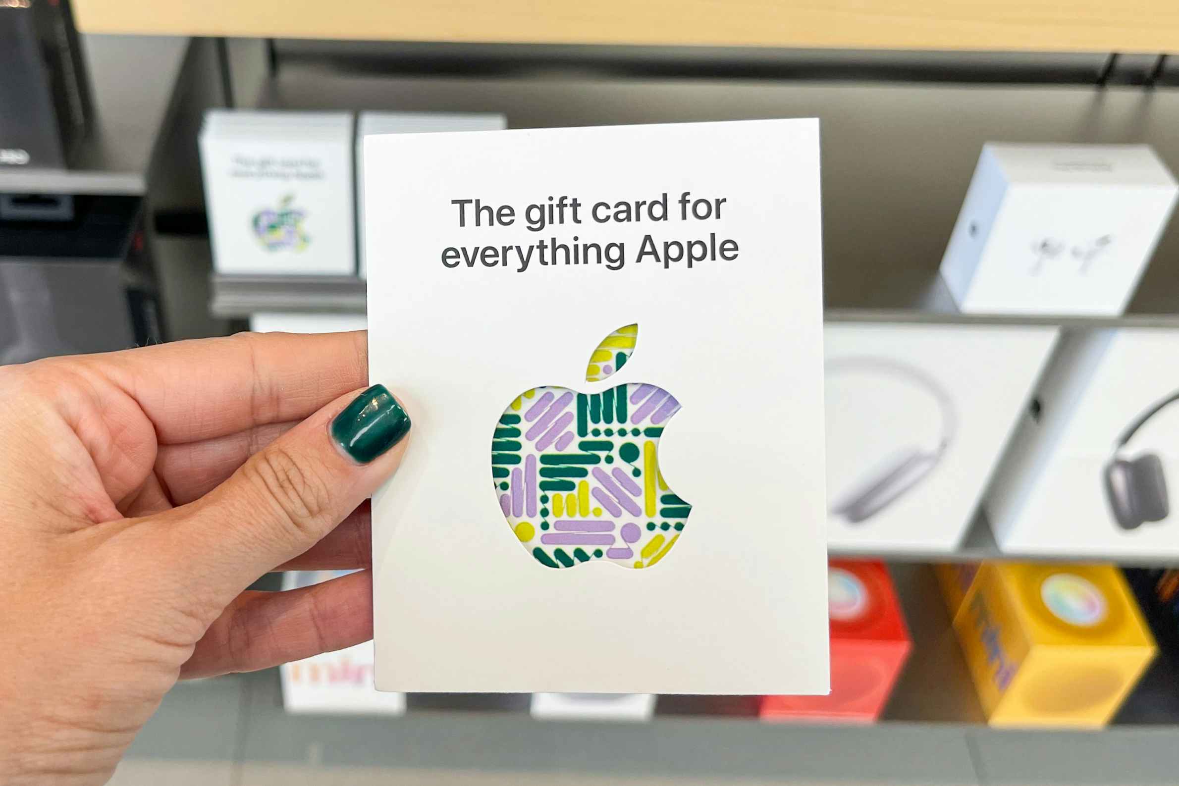 An Apple gift card held outlay hand in front of other Apple products.