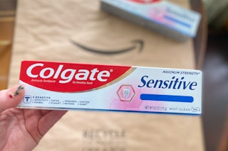 hand holding a tube of colgate sensitive toothpaste over an amazon logo package
