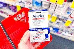 person holding a package of aquaphor healing ointment over a red basket