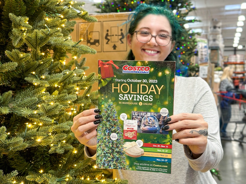 a woman holding up a costco black friday holiday savings ad in store