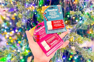 person holding 2 packs of vaseline lip therapy balms in front of a christmas tree