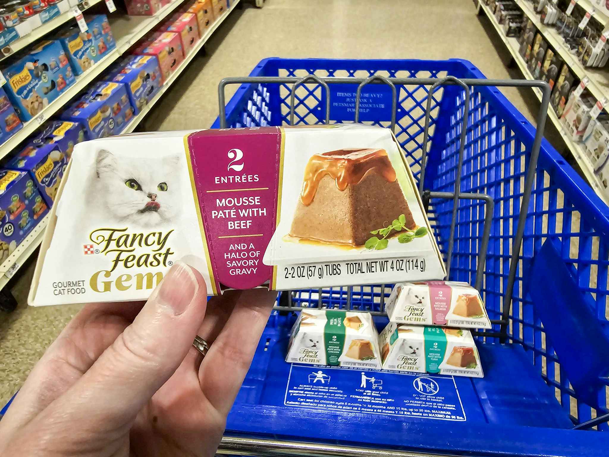 person holding a container of fancy feast cat food over a blue cart with more cat food in it