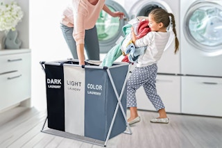 Lifestyle image of a Keenstone laundry hamper being used by a little girl and her mom in the laundry room