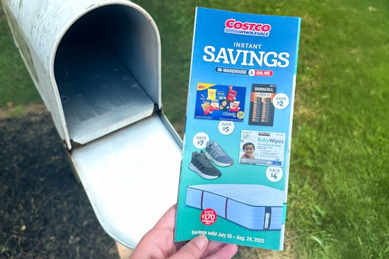 hand holding a costco coupon book july august 2025 at a mailbox