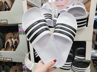 hand holding a pair of white adidas slides