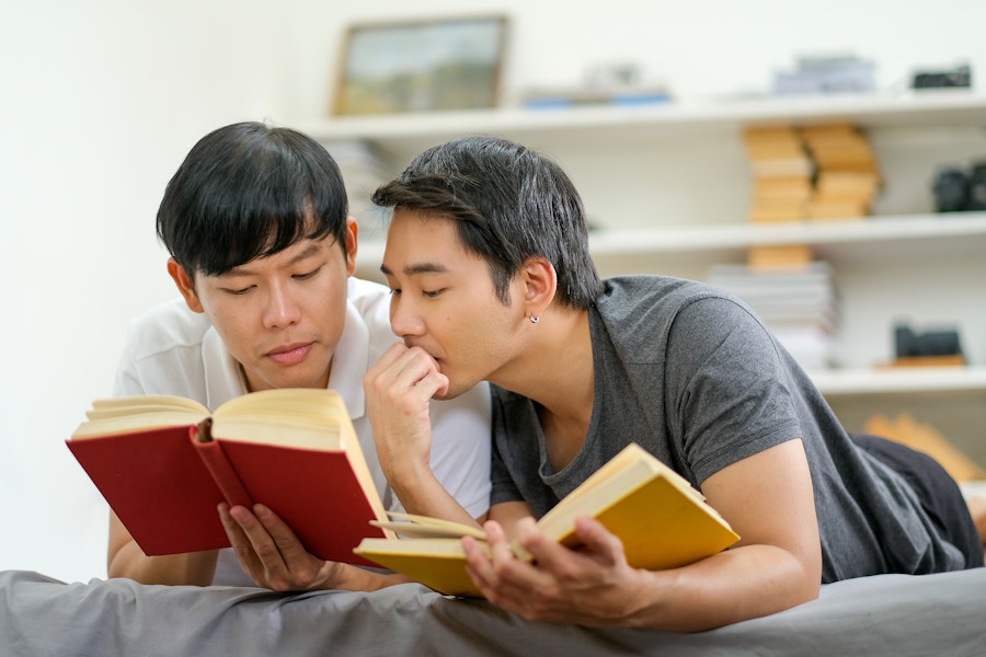 Two people laying down next to each other reading books