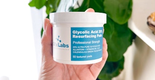 Someone holding a tub of QRx Labs Glycolic Acid pads