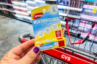 hand holding carmex weather guard lip balm next to cvs shopping cart