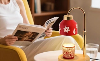 a red candle warmer lamp on a table next to a person reading