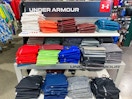 A variety of Under Armour shirts folded on a shelf in Dicks Sporting Goods