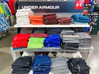 A variety of Under Armour shirts folded on a shelf in Dicks Sporting Goods