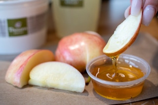 A person dipping a cut apple into honey