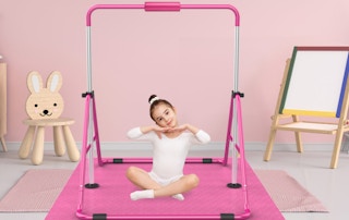a little girl sitting under a pink gymnastics bar