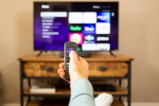 A person pointing a remote control at a TV.