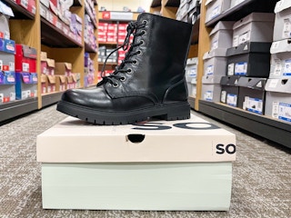 A SO combat boot sitting atop a shoe box in the middle of a store aisle.