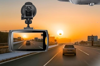 A dash camera attached to a car's window records another car at sunset
