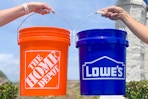 An orange Home Depot bucket and a blue Lowe's bucket held up side by side