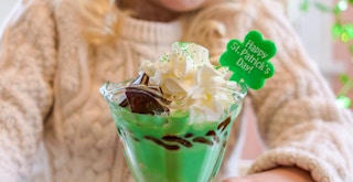 A child sitting with a green ice cream sundae that has whipped cream and a little shamrock decoration