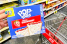 hand holding box of pop-tarts next to cvs shopping cart in grocery aisle