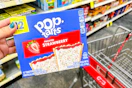 hand holding box of pop-tarts next to cvs shopping cart in grocery aisle