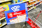 hand holding box of pop-tarts next to cvs shopping cart in grocery aisle
