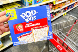 hand holding box of pop-tarts next to cvs shopping cart in grocery aisle