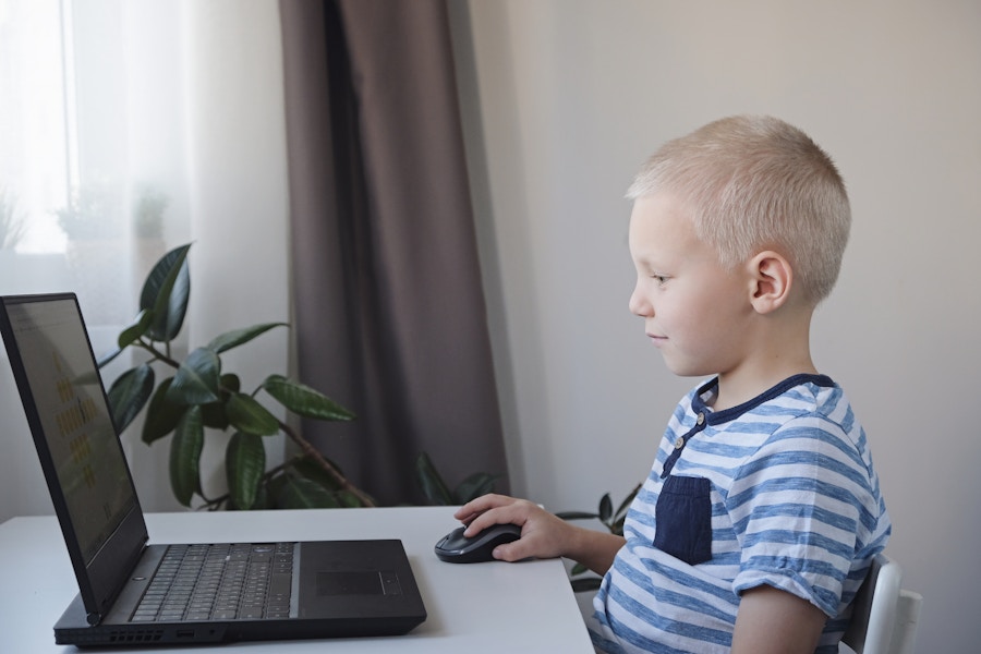 A child sitting at a table taking classes on a laptop