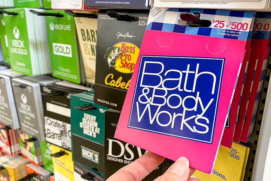 A person's hand taking a Bath & Body Works gift card from a display of gift cards at Walmart.