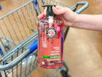 hand holding a bottle of herbal essences shampoo in front a walmart cart