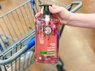 hand holding a bottle of herbal essences shampoo in front a walmart cart