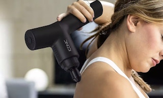 a woman using a muscle massage gun on her back