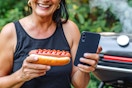 a person holding up a hot dog with ketchup and an iphone 