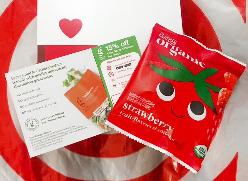 A target good and gather coupon for 15% off next to a free sample of Good & Gather strawberry fruit snacks on top of a Target plastic bag