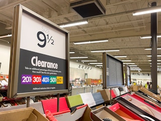 A close up of a sign for Clearance shoes, showing purple, red, blue, green, and yellow, and the discount vales that accompany each color.