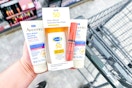 person holding aveeno healing ointment, nyx lip gloss, and cetaphil sunscreen over a walgreens cart