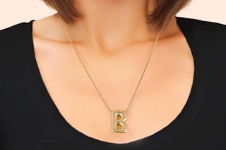 Close up of a woman wearing a goldtone bubble letter necklace